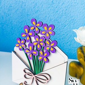 May include: A white envelope cutout featuring a bouquet of purple flowers with yellow centers and green stems, tied with a light pink bow. The text Digital Download Laser File and SVG CDR AI DXF EPS PDF Lightburn is visible on the image.