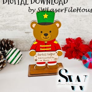Può includere: Statuetta di orso natalizio in legno con uniforme rossa e oro, cappello verde con stella gialla e un cartello con la scritta "Santa's Helper". Il testo "DIGITAL DOWNLOAD" e "by SWLaserFileHouse" sono in alto.