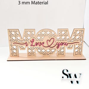 May include: A laser cut template for 3 mm material featuring the word MOM with a cane webbing pattern and a pink script overlay that reads i Love you. The design includes a flat base and text listing file formats SVG, CDR, AI, DXF, EPS, PDF, PNG, Lightburn.