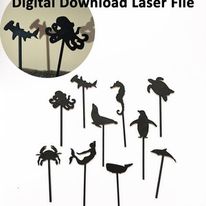 May include: A digital download of 10 black and white sea creature silhouette designs for laser cutting. The designs include a shark, octopus, seahorse, turtle, seal, penguin, crab, mermaid, whale, and a dolphin. The text "SVG - CDR - AI - DXF - EPS - PDF - PNG - Lbrn2" is repeated twice at the bottom of the image.