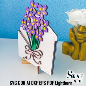 May include: A laser-cut wooden craft project featuring a white envelope with a bouquet of purple flowers with yellow centers and a pink bow. The text reads Digital Download Laser File and SVG CDR AI DXF EPS PDF Lightburn.