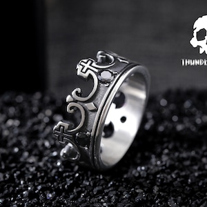 May include: A silver ring with a crown design featuring black gemstones. The ring is on a black background.