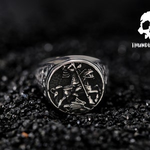 May include: A silver ring featuring an intricate design of a knight on horseback. The ring is displayed against a black backdrop.