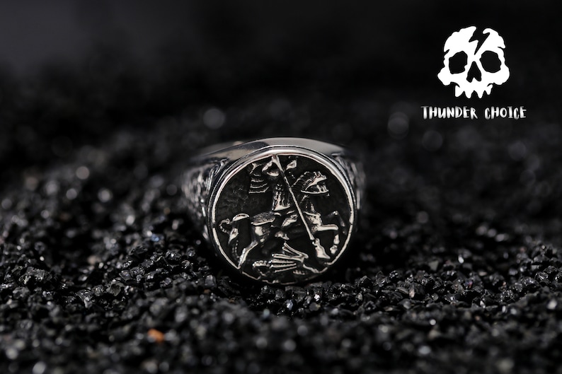 May include: A silver ring featuring an intricate design of a knight on horseback. The ring is displayed against a black backdrop.