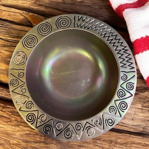 May include: A silver bowl with a black iridescent finish and a decorative border of swirls and zigzags.