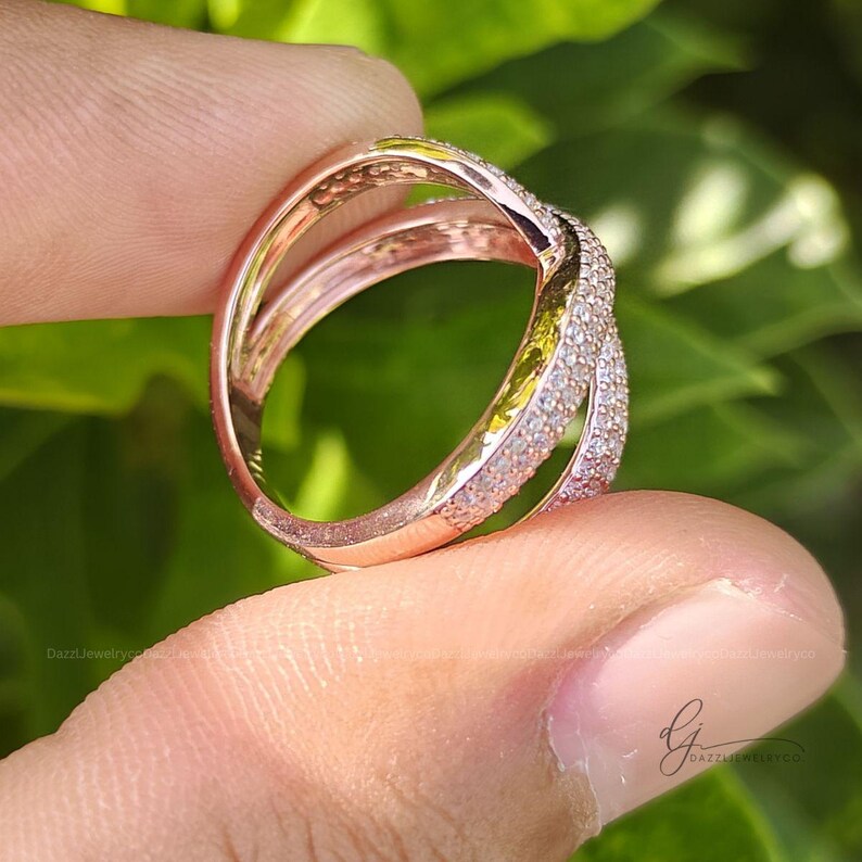 May include: A rose gold ring featuring a crossover band design with two intersecting shanks. One shank is smooth and polished, while the other is encrusted with small, clear pav&eacute;-set stones that catch the light, creating a textured appearance.