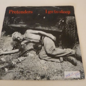 May include: Black and white photo of a young person sleeping on the ground. The photo is a record cover for the song "I go to sleep" by The Pretenders.