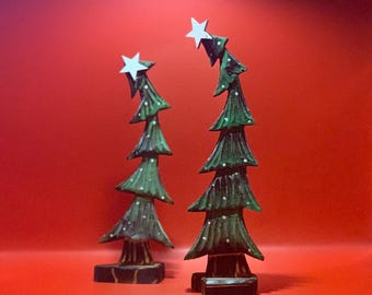 May include: Two wooden Christmas trees with white stars on top. The trees are green and have a wood grain texture. They are standing on a red surface.