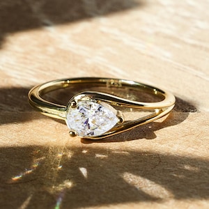 May include: A gold ring with a pear-shaped diamond set in a delicate, twisted band.
