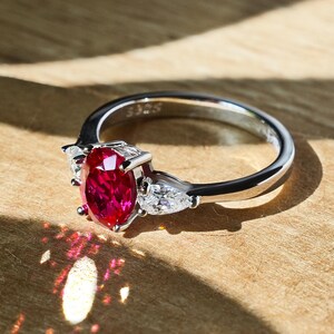 Könnte beinhalten: Ein silberner Ring mit einem großen ovalen Rubin-Edelstein und zwei kleineren birnenförmigen Diamanten auf jeder Seite.