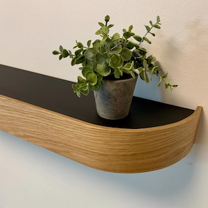 Peut inclure: Une étagère en bois incurvée avec un dessus noir. Une petite plante en pot est posée sur l'étagère.