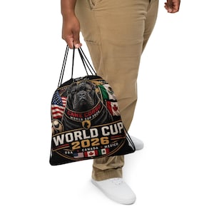 May include: A black drawstring bag featuring a graphic of a Cane Corso dog, the text "WORLD CUP 2026", and the flags of the USA, Canada, and Mexico. The design includes a soccer ball and the words "CANE CORSO WORLD CUP 2026" in a circular emblem.