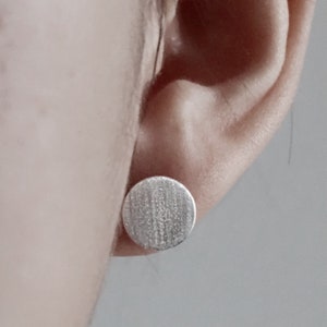 Può includere: Un paio di orecchini a bottone in argento con un design circolare. Gli orecchini hanno una superficie testurizzata.