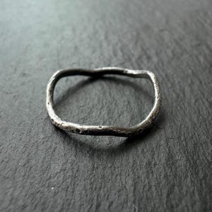 Könnte beinhalten: Ein silberfarbener Ring mit einer unregelmäßigen, organischen Form. Der Ring hat eine strukturierte Oberfläche und ein leicht unebenes Band. Das Design ist minimalistisch und modern. Der Ring hat einen Durchmesser von ca. 1,9 cm.