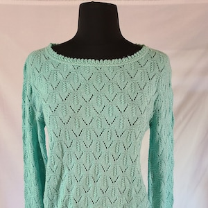 May include: A light green knitted sweater with a delicate openwork pattern. The sweater has a round neckline and long sleeves.