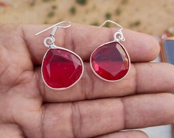 Peut inclure: Une paire de boucles d'oreilles pendantes en argent avec des gouttes de pierres précieuses rouges. Les boucles d'oreilles ont une forme de larme et sont faites d'un métal brillant.