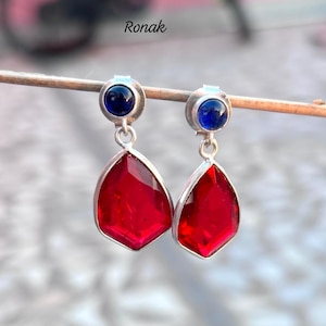 Peut inclure: Une paire de boucles d'oreilles en argent avec des accents de pierres précieuses rouges et bleues. Les boucles d'oreilles présentent une pierre précieuse rouge en forme de larme avec une plus petite pierre précieuse bleue en haut.