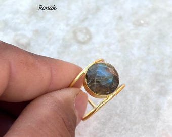 Può includere: Anello in oro con una grande pietra rotonda di labradorite iridescente incastonata in un design a doppia fascia.