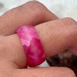Puede incluir: Un anillo facetado rosa hecho de resina. El anillo se lleva en un dedo.