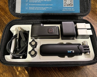 May include: A black GoPro camera, two black batteries, a black charging cable, two black thumb screws, a black GoPro selfie stick, and a blue and white instruction booklet are inside a black carrying case.