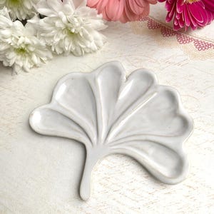 Peut inclure: Un plat en céramique blanche en forme de feuille de ginkgo. Le plat a un design en relief texturé et est parfait pour servir de petites collations ou des bijoux.