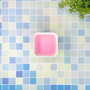 Pode incluir: Uma tigela quadrada branca cheia de líquido rosa sobre um fundo de azulejos.