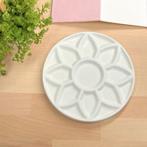 Può includere: Paletta per pittura in ceramica bianca con 12 pozzetti a forma di fiore. La paletta è rotonda e ha un bordo rialzato.