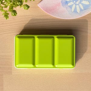 Könnte beinhalten: Eine limettengrüne Metall-Farbpalette mit drei leeren Vertiefungen.