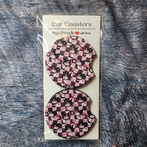 May include: Two round black and pink car coasters with a checkered pattern and a cartoon character design. The coasters are packaged in a clear plastic bag with a white card that says "Car Coasters Handmade with love".
