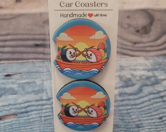 May include: Two round car coasters with a sunset background and a cartoon image of two sushi rolls in a boat. The text "Car Coasters" and "Handmade with love" is printed on the packaging.
