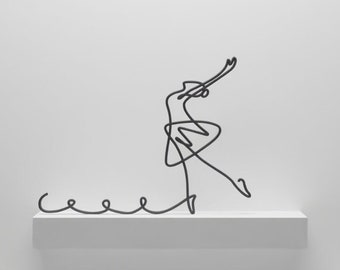 May include: A minimalist home decor arrangement featuring a black wire sculpture of a ballerina on a white shelf. Two white, abstract vases with green plants are on lower shelves, creating a balanced, modern aesthetic.