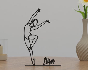 May include: Black metal wire sculpture of a ballerina in a dance pose with the name "Eliza" written below.