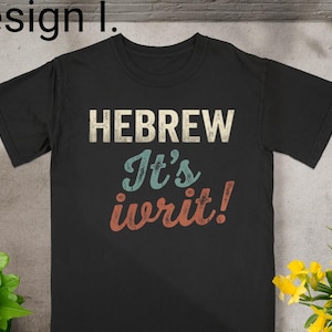 May include: A black short-sleeved t-shirt featuring the text "Design 1." at the top left. The center of the shirt displays the text "HEBREW" in a distressed white font, followed by "It's" in light blue and "ivrit!" in a distressed red font.