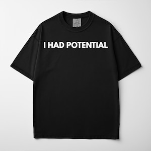 May include: Black short-sleeved t-shirt with the white text "I HAD POTENTIAL" across the chest. The shirt has a crew neck and a small tag at the neckline. The shirt is made of a soft material.