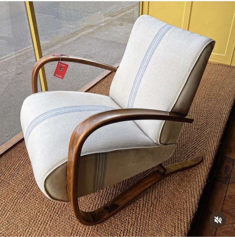May include: A white armchair with blue stripes on the fabric upholstery. The chair has a wooden frame and a curved design. The chair is sitting on a brown woven rug.