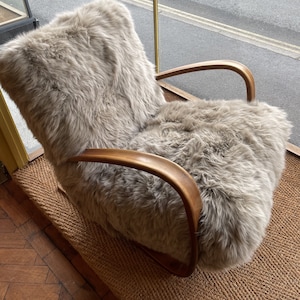 May include: A light brown, sheepskin-covered armchair with wooden arms. The chair is sitting on a woven rug.