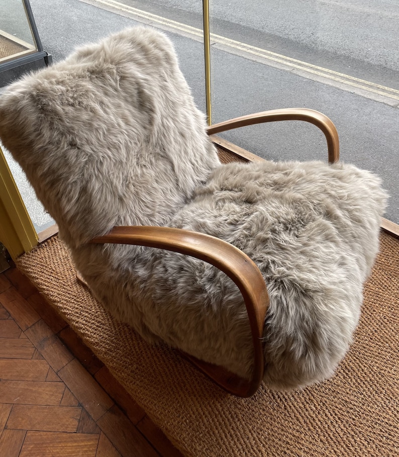 May include: A light brown, sheepskin-covered armchair with wooden arms. The chair is sitting on a woven rug.