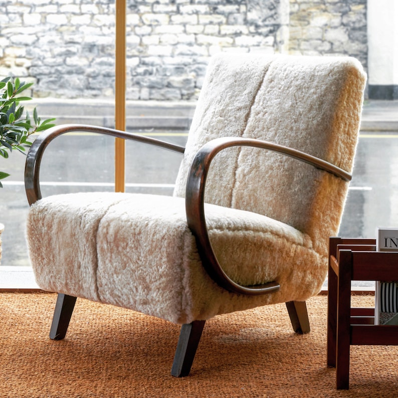 May include: A white sheepskin armchair with wooden arms and legs. The chair is sitting on a brown rug.