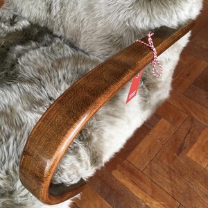 May include: A close-up of a wooden armrest of a chair with a light gray sheepskin covering. The armrest is curved and has a smooth, polished finish. A red and white string is tied around the armrest.