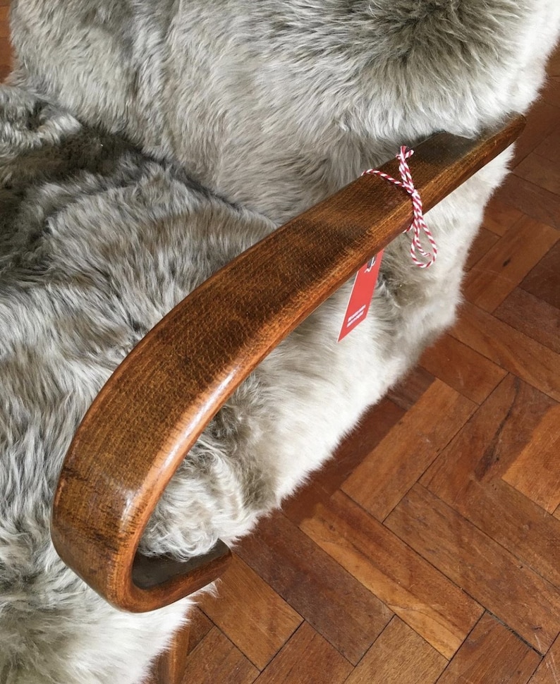 May include: A close-up of a wooden armrest of a chair with a light gray sheepskin covering. The armrest is curved and has a smooth, polished finish. A red and white string is tied around the armrest.