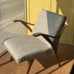 May include: A gray upholstered armchair with wooden arms and legs. The chair is sitting on a woven rug.