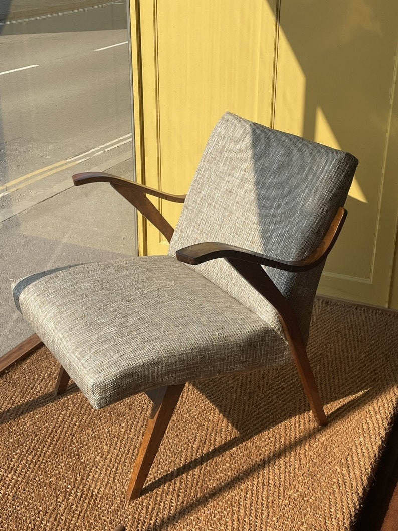 May include: A gray upholstered armchair with wooden arms and legs. The chair is sitting on a woven rug.