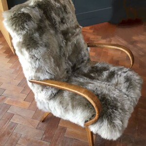 May include: A brown faux fur armchair with wooden arms and legs. The chair is on a wooden floor.