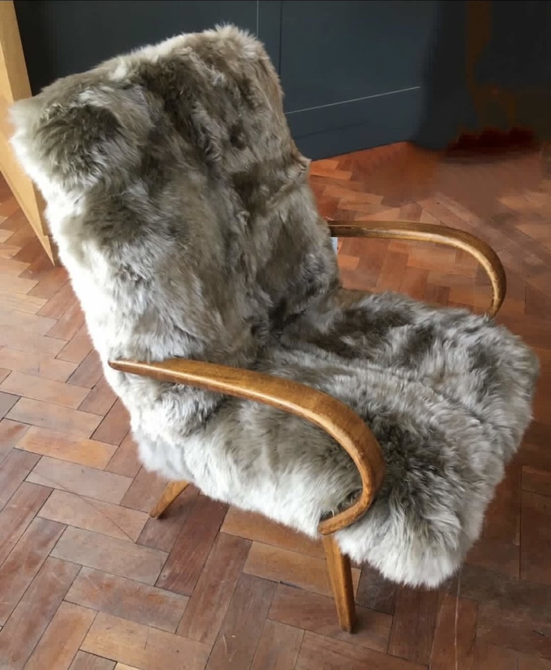 May include: A brown faux fur armchair with wooden arms and legs. The chair is on a wooden floor.