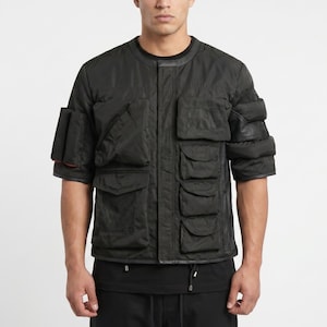 May include: Black short-sleeved jacket with multiple pockets. The jacket has a round collar and a quilted design. The sleeves have a unique layered design. The jacket is made of a matte material.