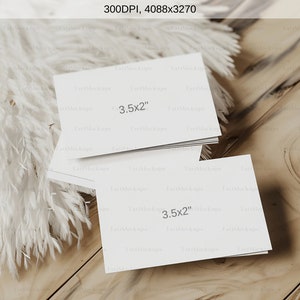 May include: A stack of white rectangular cards, each measuring 3.5 x 2 inches, rests on a light wood surface. Fluffy white decorative elements are arranged to the left. The image is well-lit, showcasing the cards' clean design.