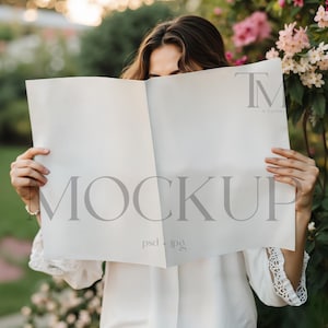 May include: A woman holds a white sheet of paper in front of her face. The paper has the word "MOCKUP" printed on it in a gray font. The woman is wearing a white shirt and has long brown hair.