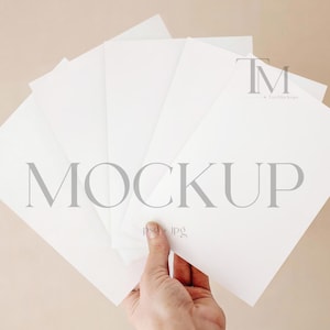 Op de afbeelding: Een mockup met een hand die een waaier van witte kaarten vasthoudt tegen een neutrale achtergrond. Het woord "MOCKUP" wordt in lichtgrijze letters over de kaarten weergegeven. De afbeelding is een platte lay-out.