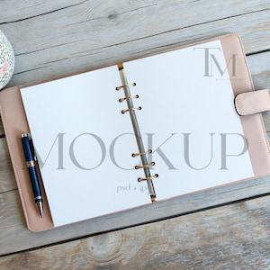 May include: A light pink leather planner with a gold-colored binder and a matching pen. The planner is open to blank white pages with the word "MOCKUP" printed in gray. A floral patterned mug is in the upper left corner.