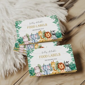 May include: A stack of food labels with a jungle theme. The labels feature illustrations of a hippo, elephant, giraffe, lion, and zebra. The text "fully editable FOOD LABELS ADD YOUR OWN TEXT" is printed on the labels.